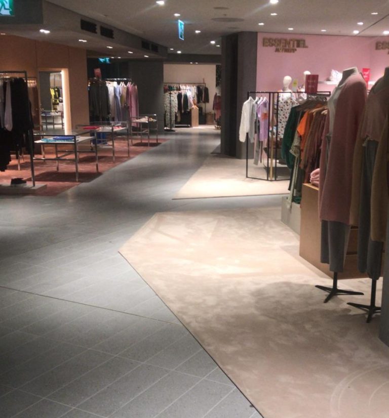 Ein modernes Bekleidungsgeschäft mit Regalen und Kleiderständern auf hellem Boden.